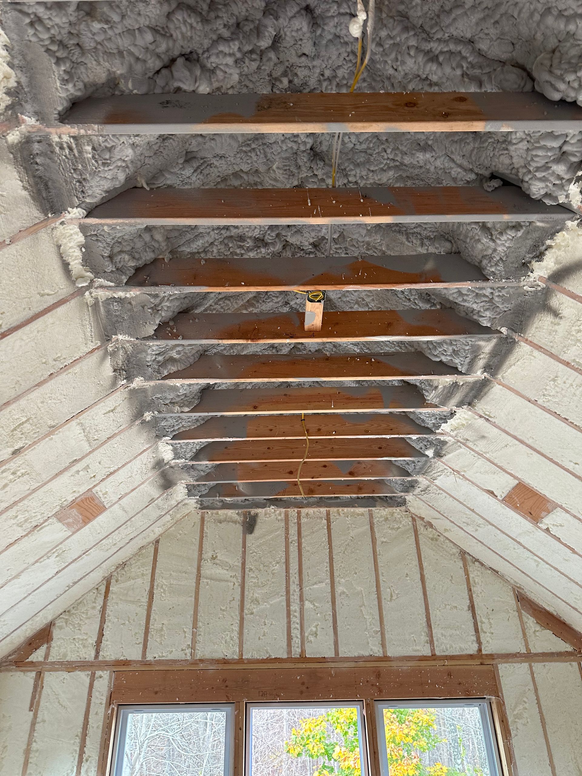Interior view of a roof with exposed wooden beams and insulation, revealing framing and window below.