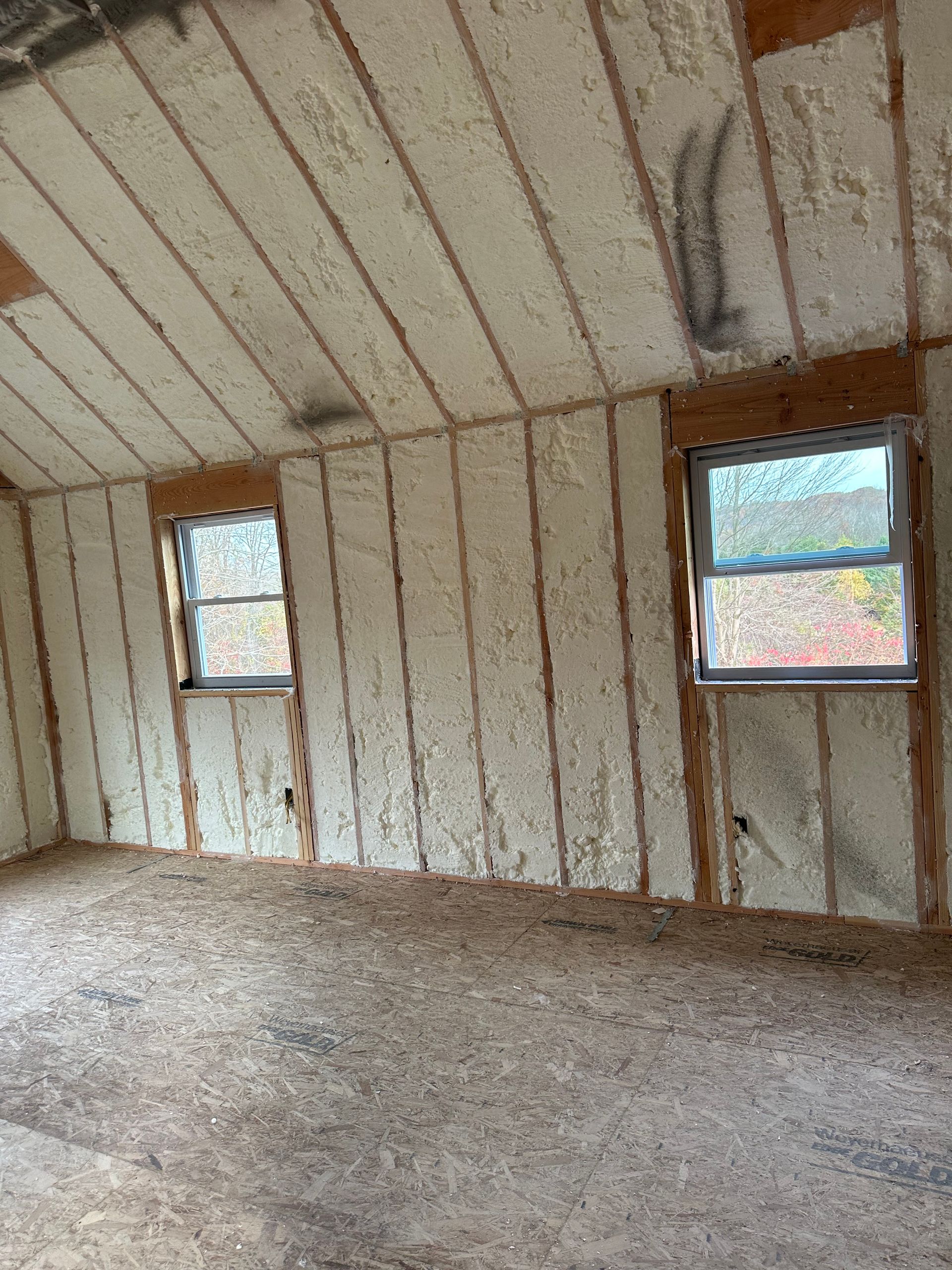 Interior view of a room with spray foam insulation visible on walls and ceiling, two windows.