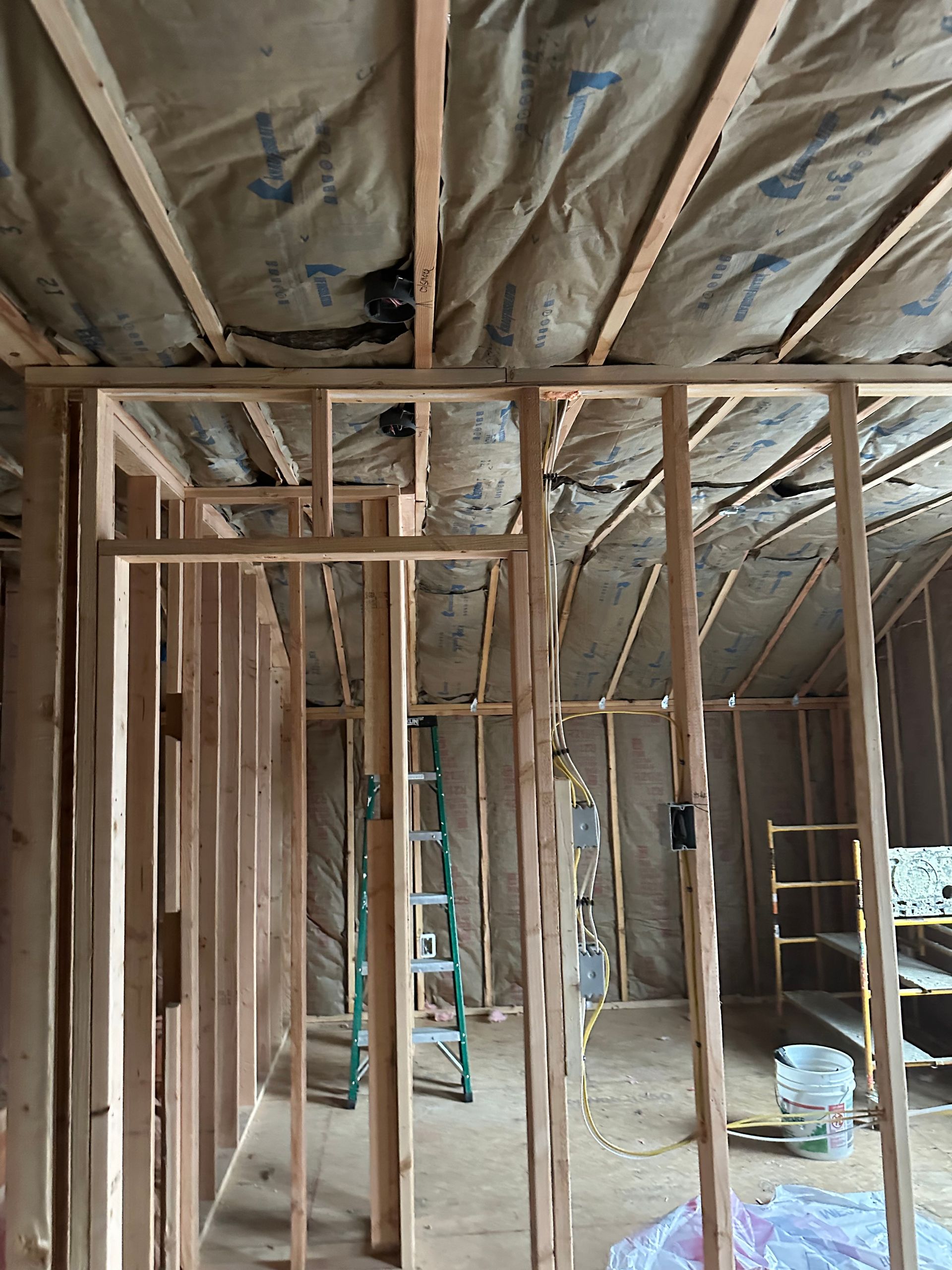 Interior framing of a new room under construction. Exposed wooden studs, insulation, and electrical boxes visible.