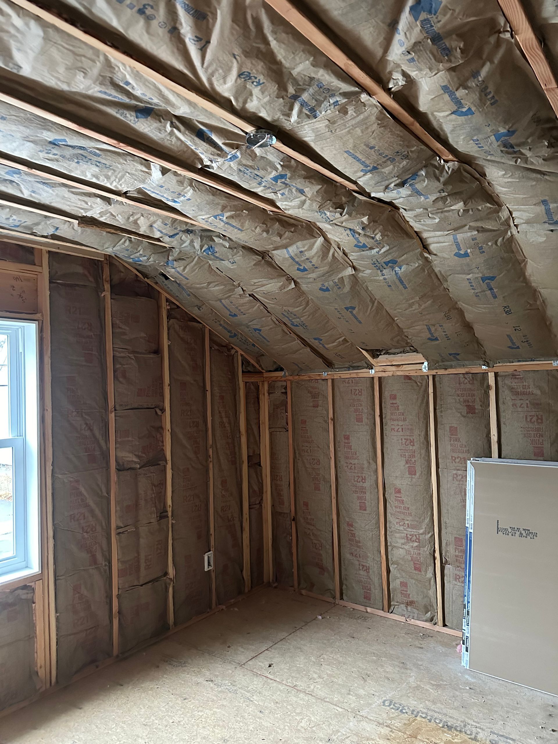 Interior of a room under construction, showing wooden framing and insulation between studs and rafters.