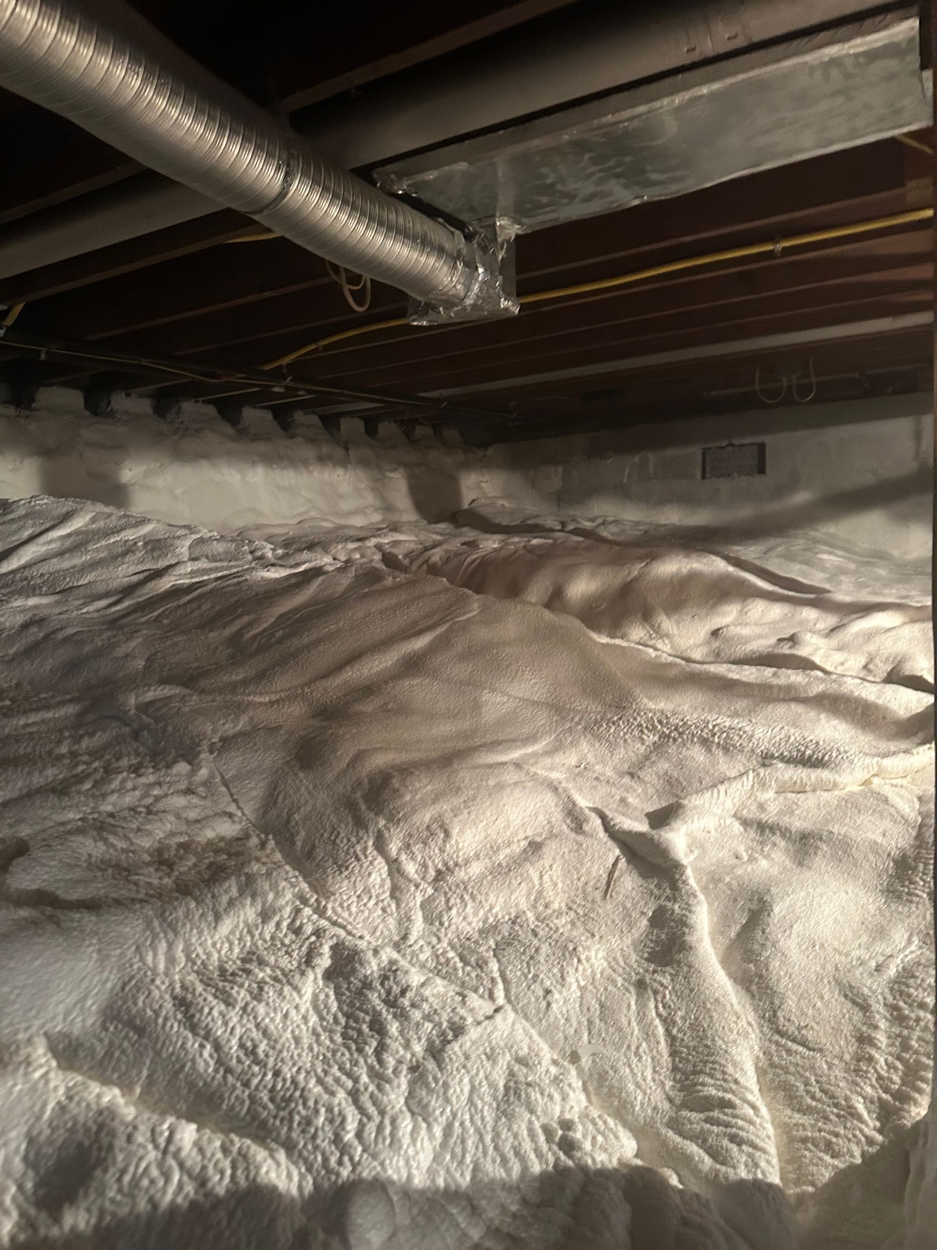 Insulation in a crawl space, with ductwork and support beams visible above.