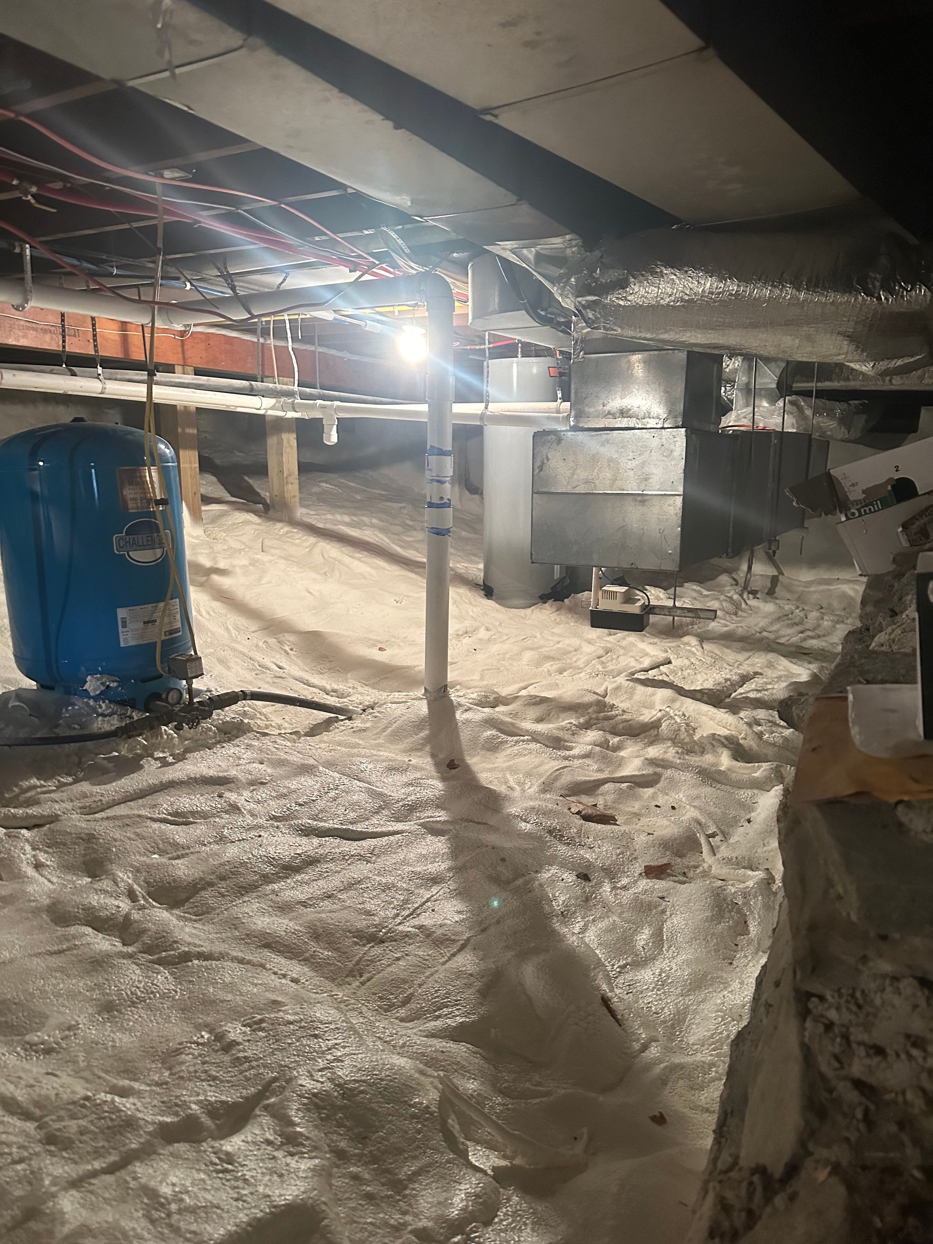 Crawl space with blue water tank, insulation, ductwork, and support beams. Bright overhead light.