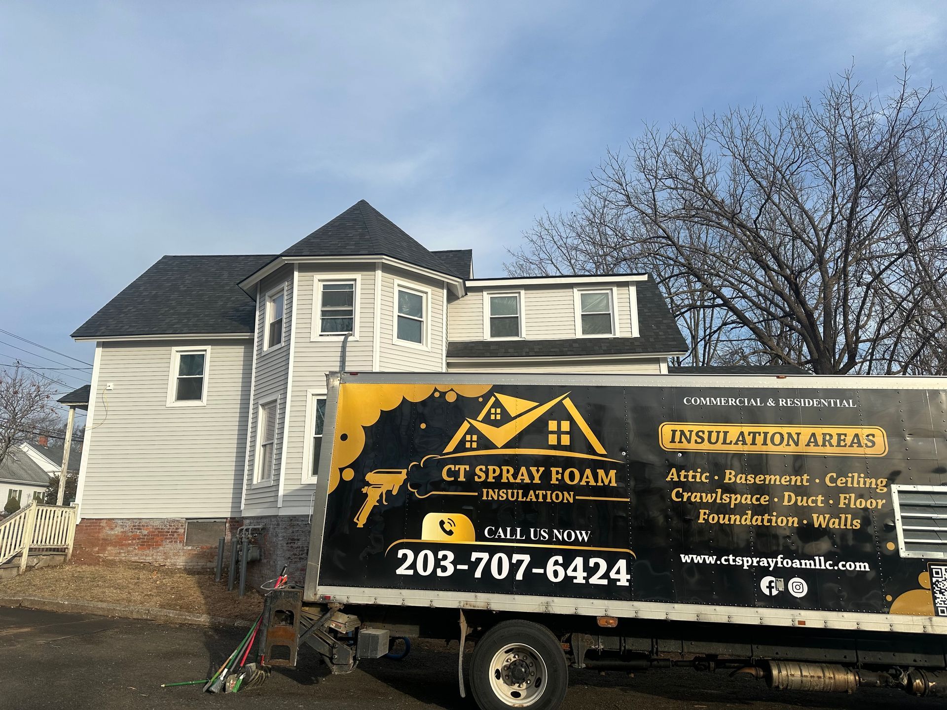 Spray foam truck parked in front of a house. The truck displays company name and phone number. The house has gray siding.