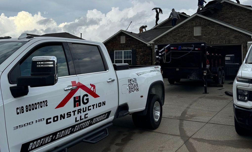 White RG Construction truck in front of a house with workers on the roof, cloudy sky.