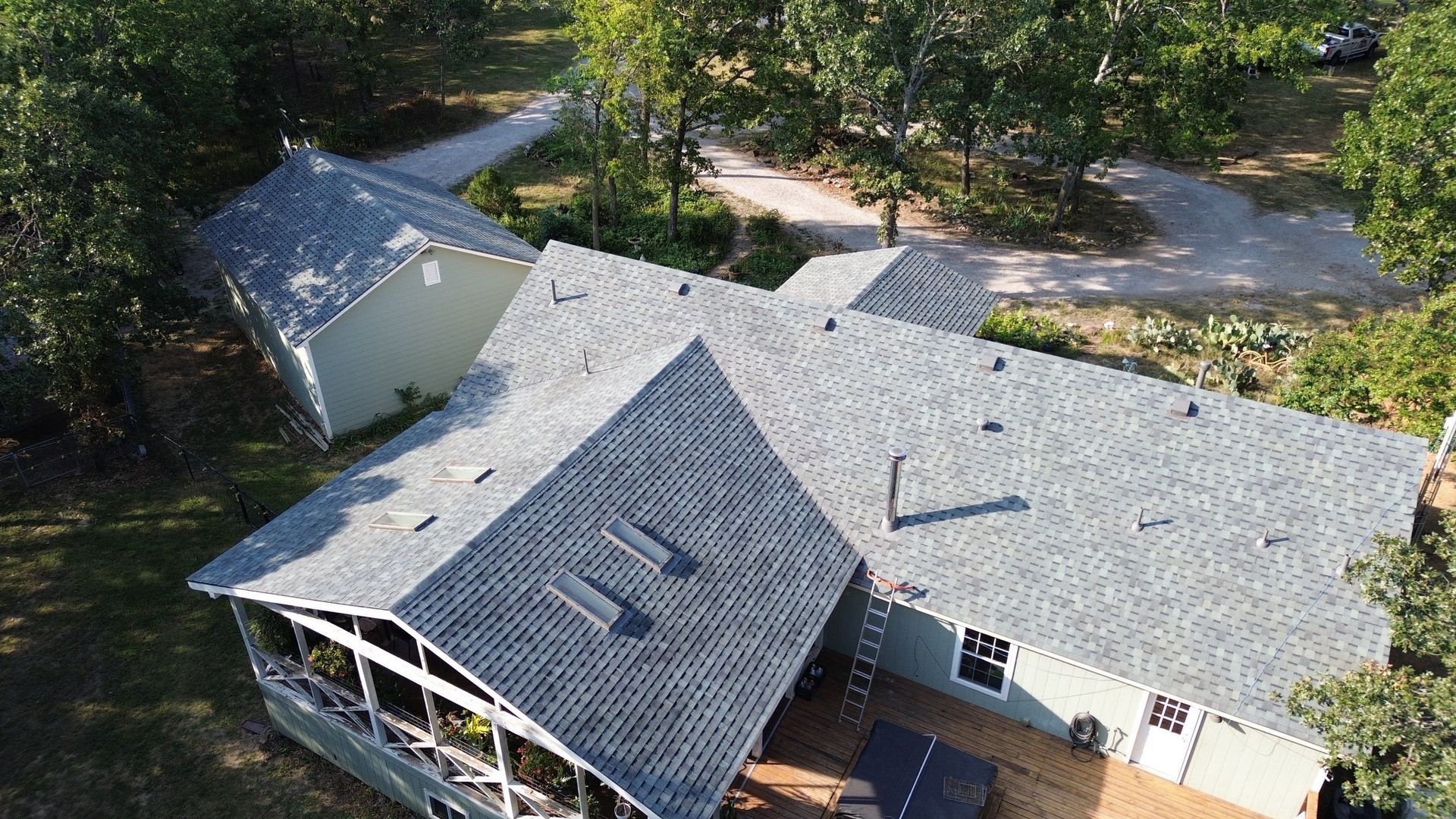 Aerial view of a light green house with gray roofs and a deck surrounded by trees.