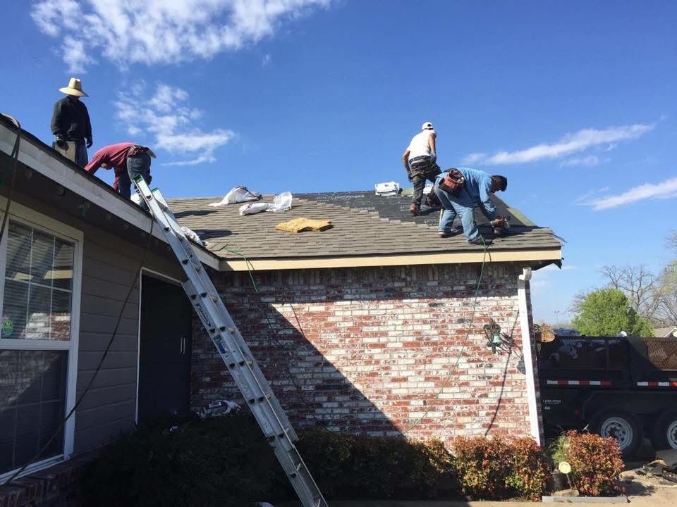 Roofers replacing shingles on a house under a clear blue sky. A ladder is propped against the roof.