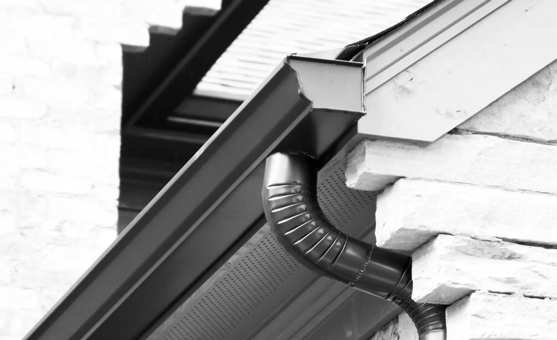 Black gutter and downspout on a building with white brick and wood siding.
