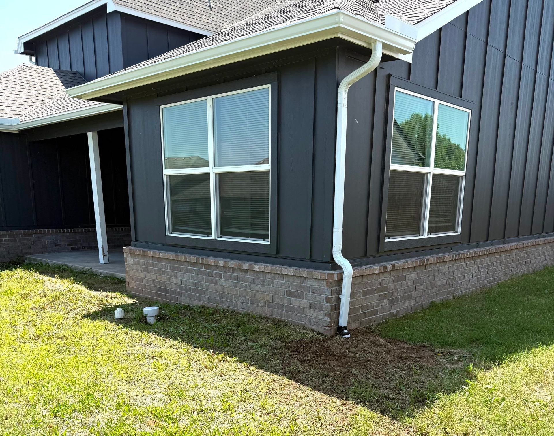 Black building exterior with two large windows on a brick base and white trim, with green grass in foreground.