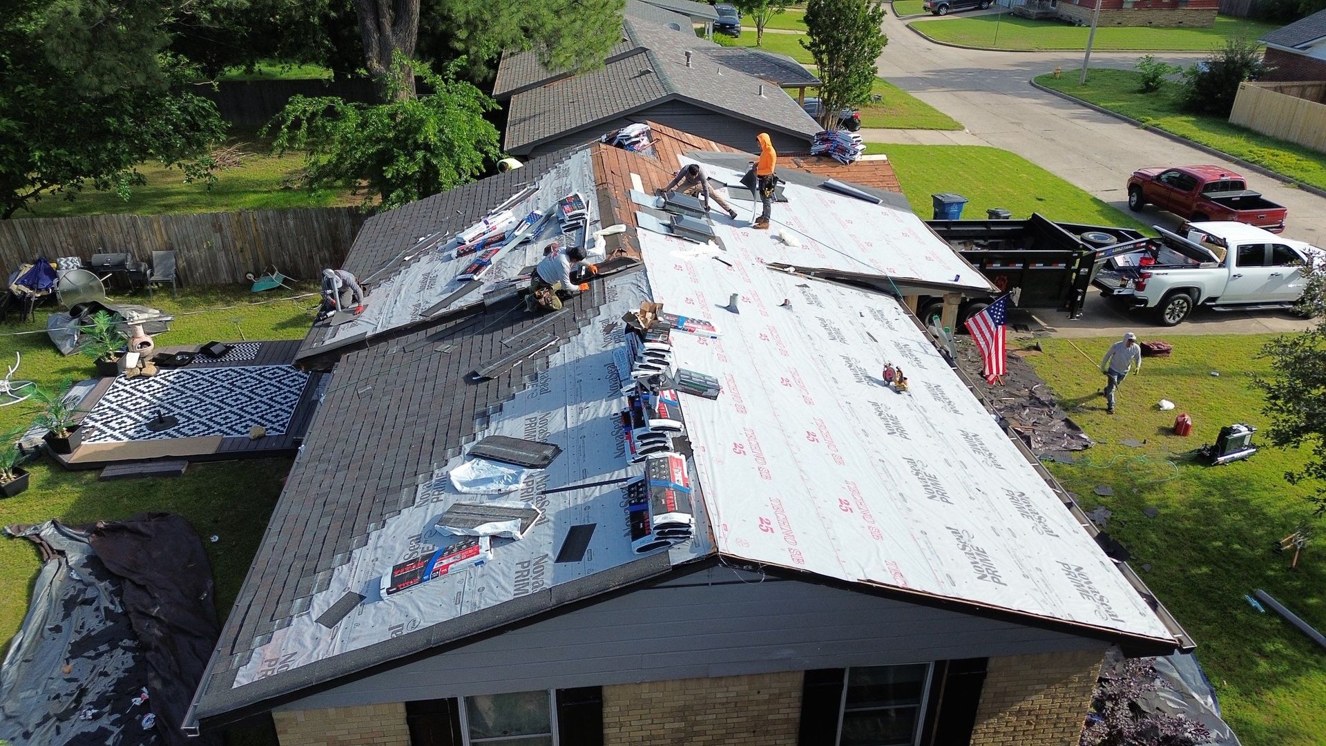 Roofers replace a shingle roof on a house with an American flag.