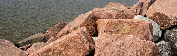 Large, reddish-brown rocks line the edge of a calm, dark body of water.