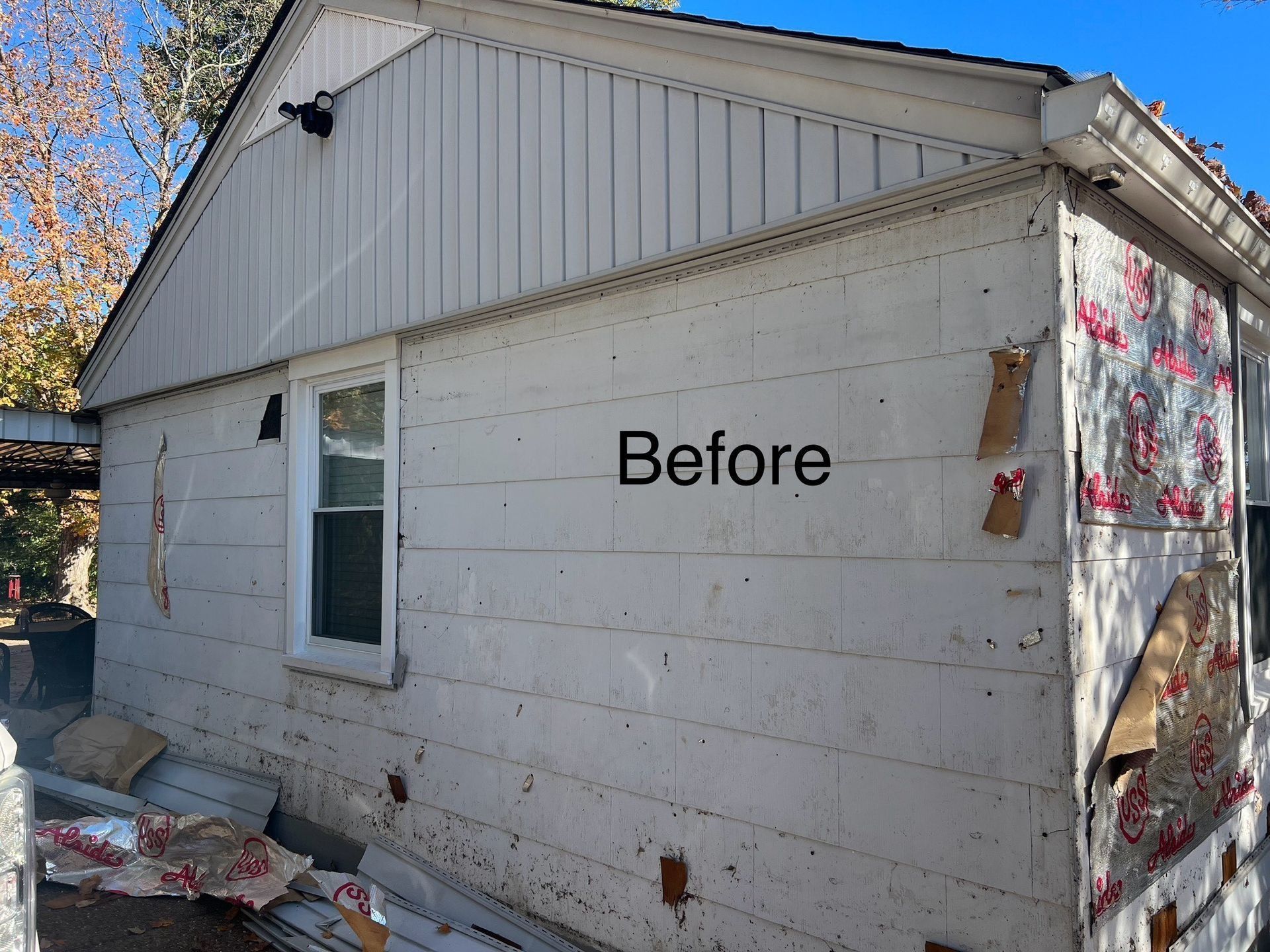 Side of a weathered white house with boarded-up windows; the word 
