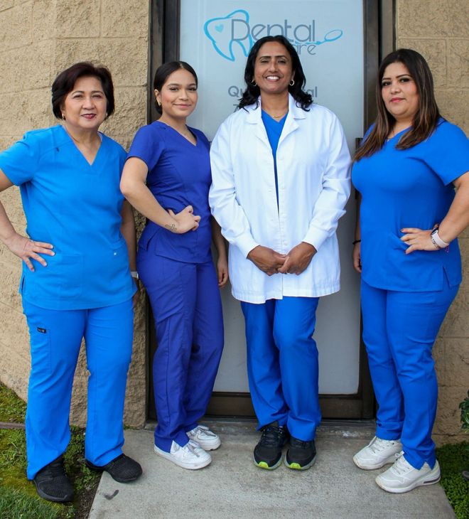 Four dental staff in blue scrubs and a white coat pose in front of a clinic entrance.