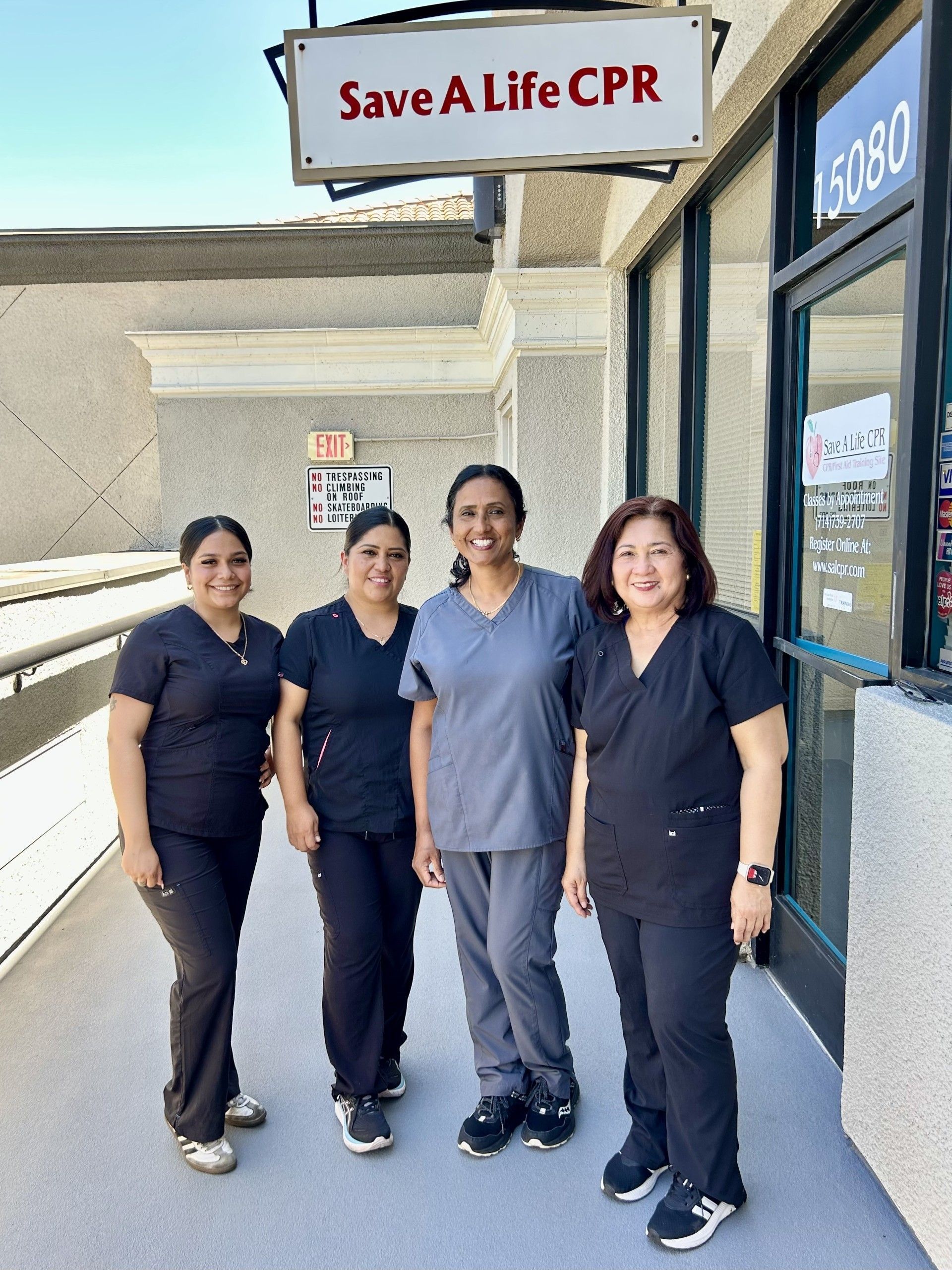 Four people in navy scrubs stand outside a CPR training center sign.