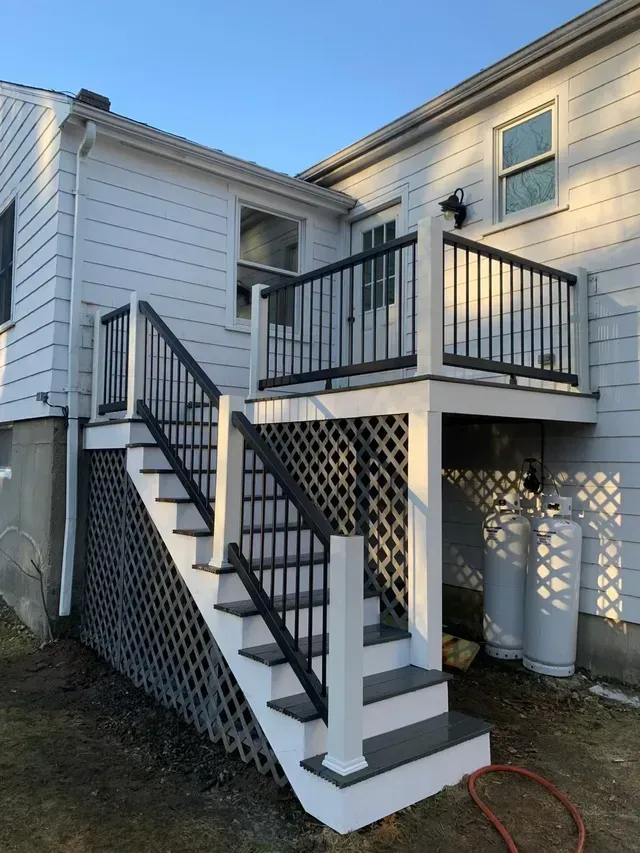 A white house with stairs leading up to a deck.