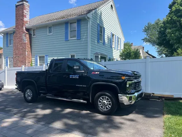 A black truck is parked in front of a house with a white fence.
