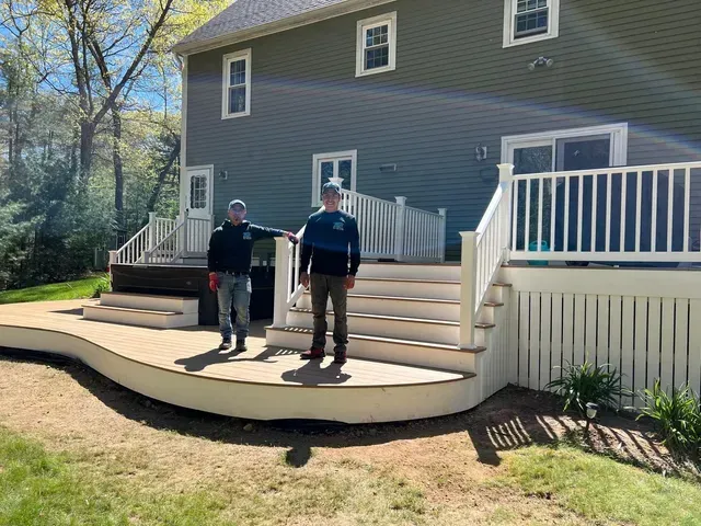 Two men are standing on a deck in front of a house.