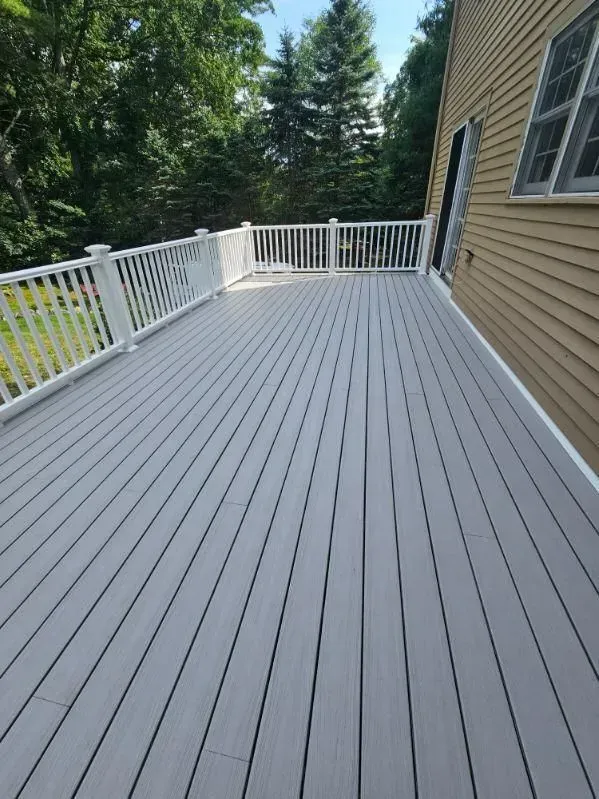 A large gray deck with a white railing and trees in the background.