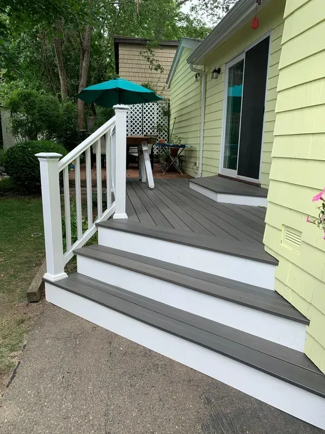 A deck with a table and umbrella on it in front of a house.