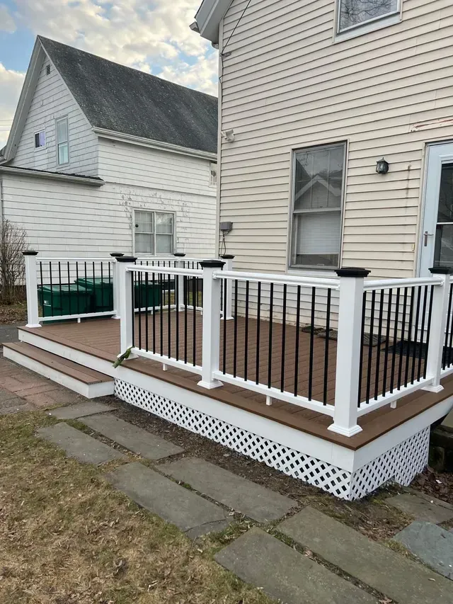 A deck with a white railing is in front of a house.