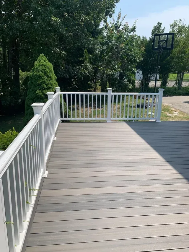 A deck with a white railing and a basketball hoop in the background.