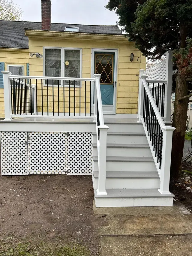 A yellow house with a white deck and stairs leading up to it.