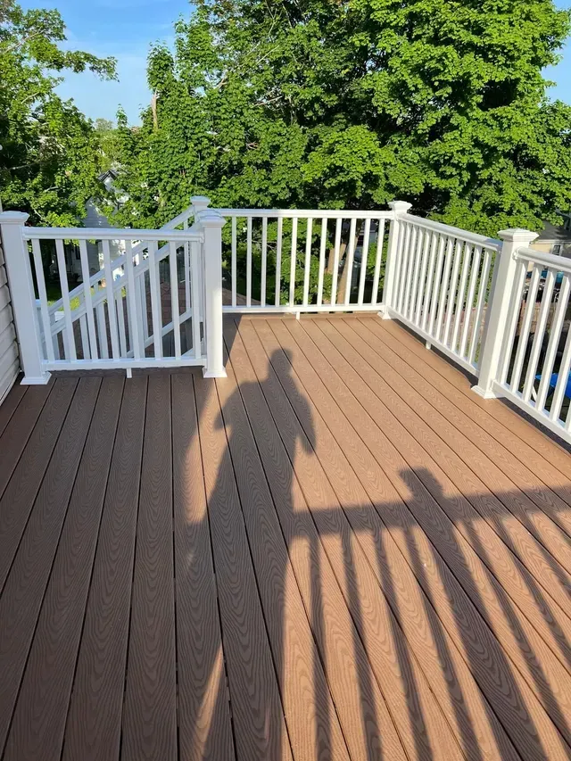 A wooden deck with a white railing and trees in the background.