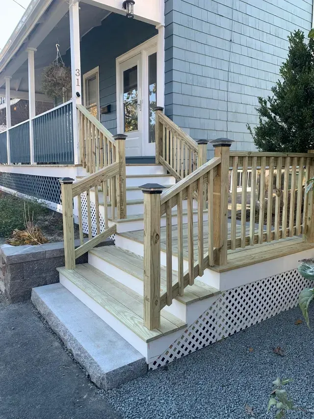 A wooden deck with stairs leading up to the front door of a house.
