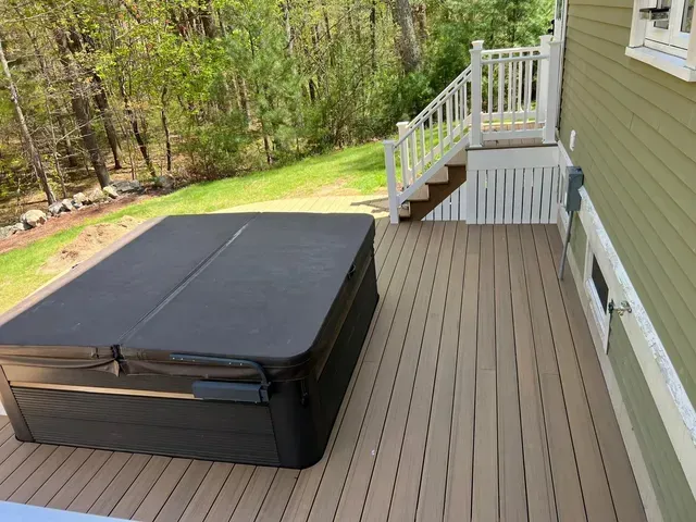 A hot tub is sitting on a wooden deck next to a house.