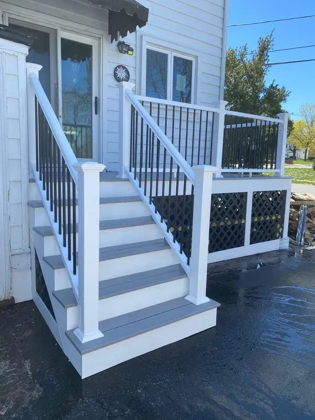 A white house with a black railing and stairs.