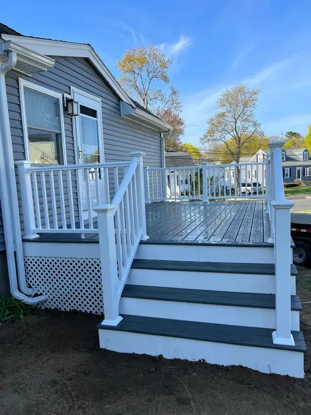 A deck with stairs and a white railing on the side of a house.