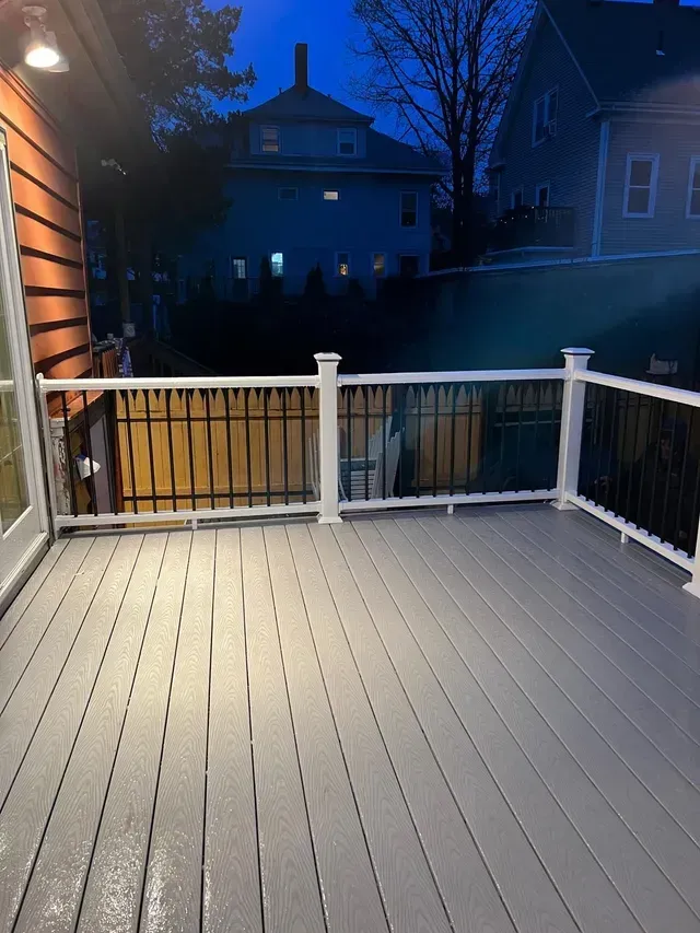 A gray deck with a white railing is lit up at night.