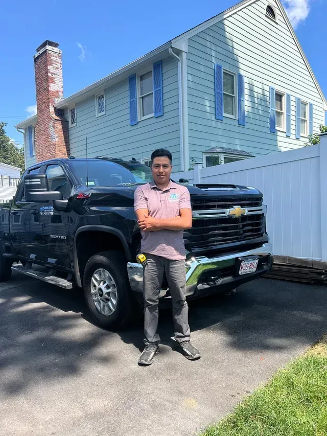 A man is standing in front of a truck in front of a house.