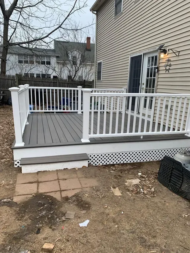 A deck with a white railing is in front of a house.