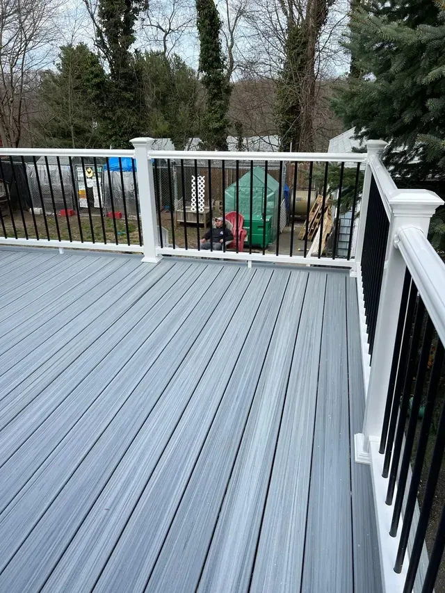 A gray deck with a white railing and trees in the background.
