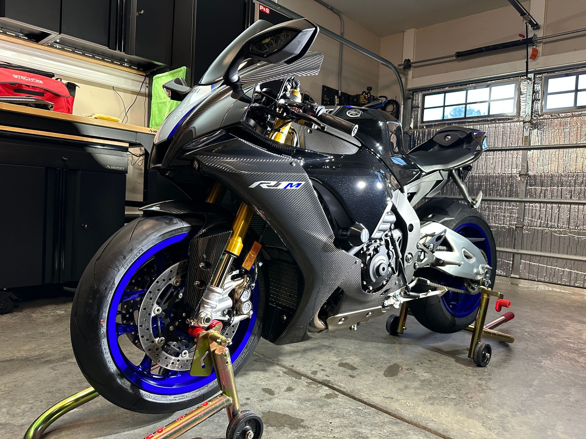 Black Yamaha R1 motorcycle with blue wheels on a stand inside a garage.