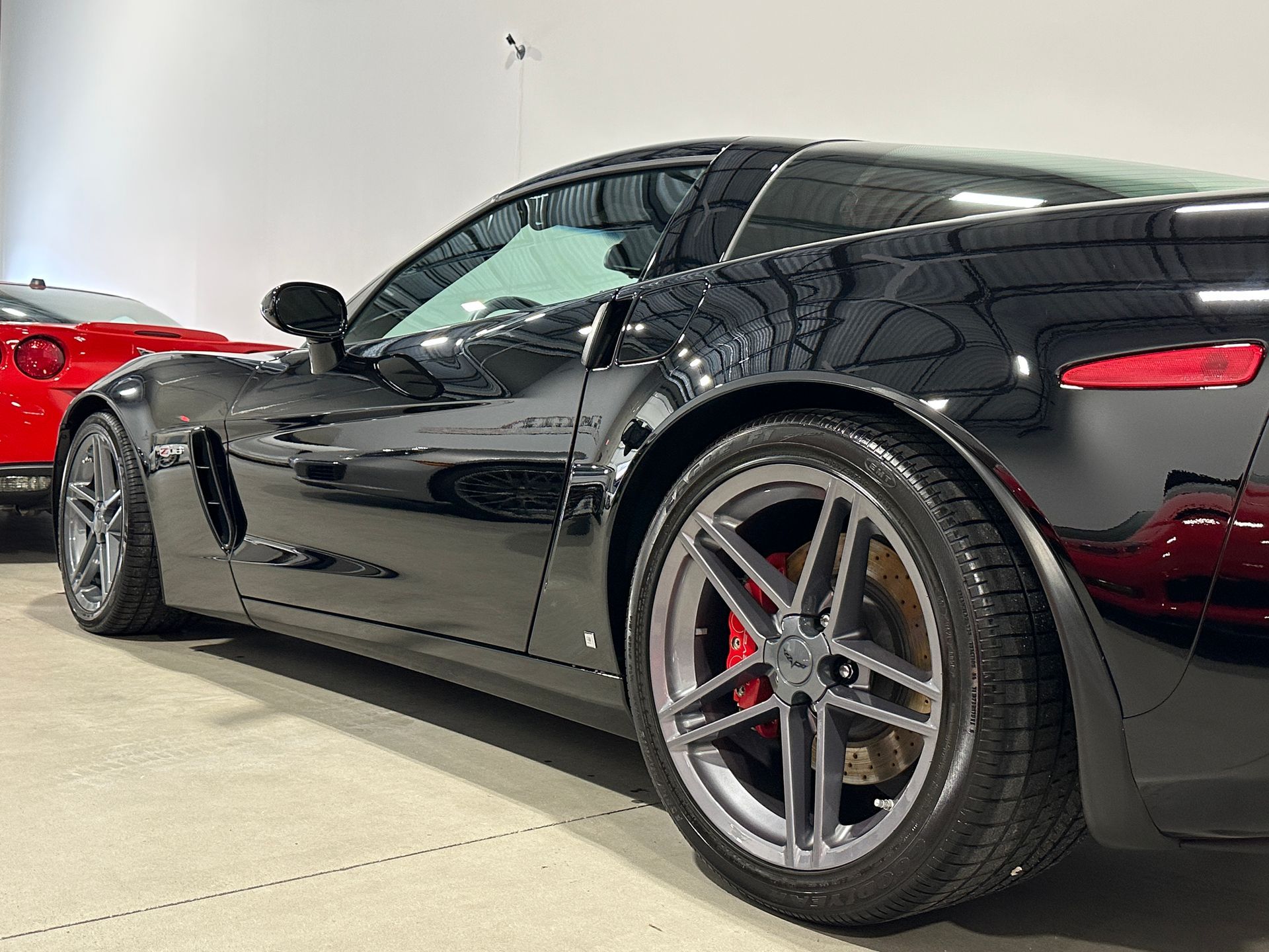 Black Corvette sports car with gray wheels and red brake calipers, parked indoors.