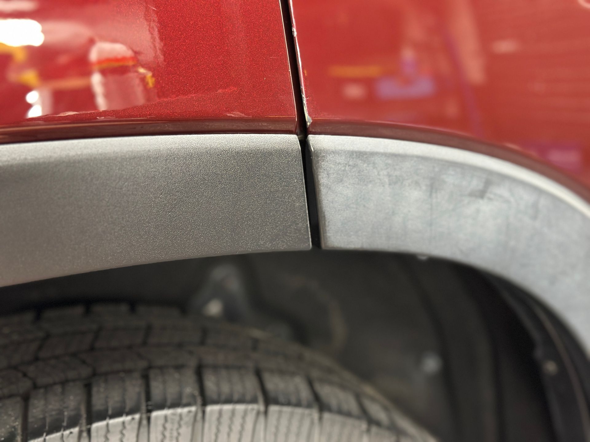 Close-up of a red car door and black fender with a gap, near a tire.