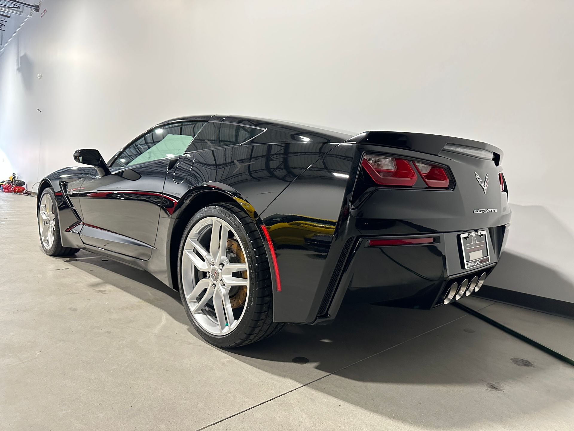 Black Chevrolet Corvette sports car in a showroom, angled rear view.