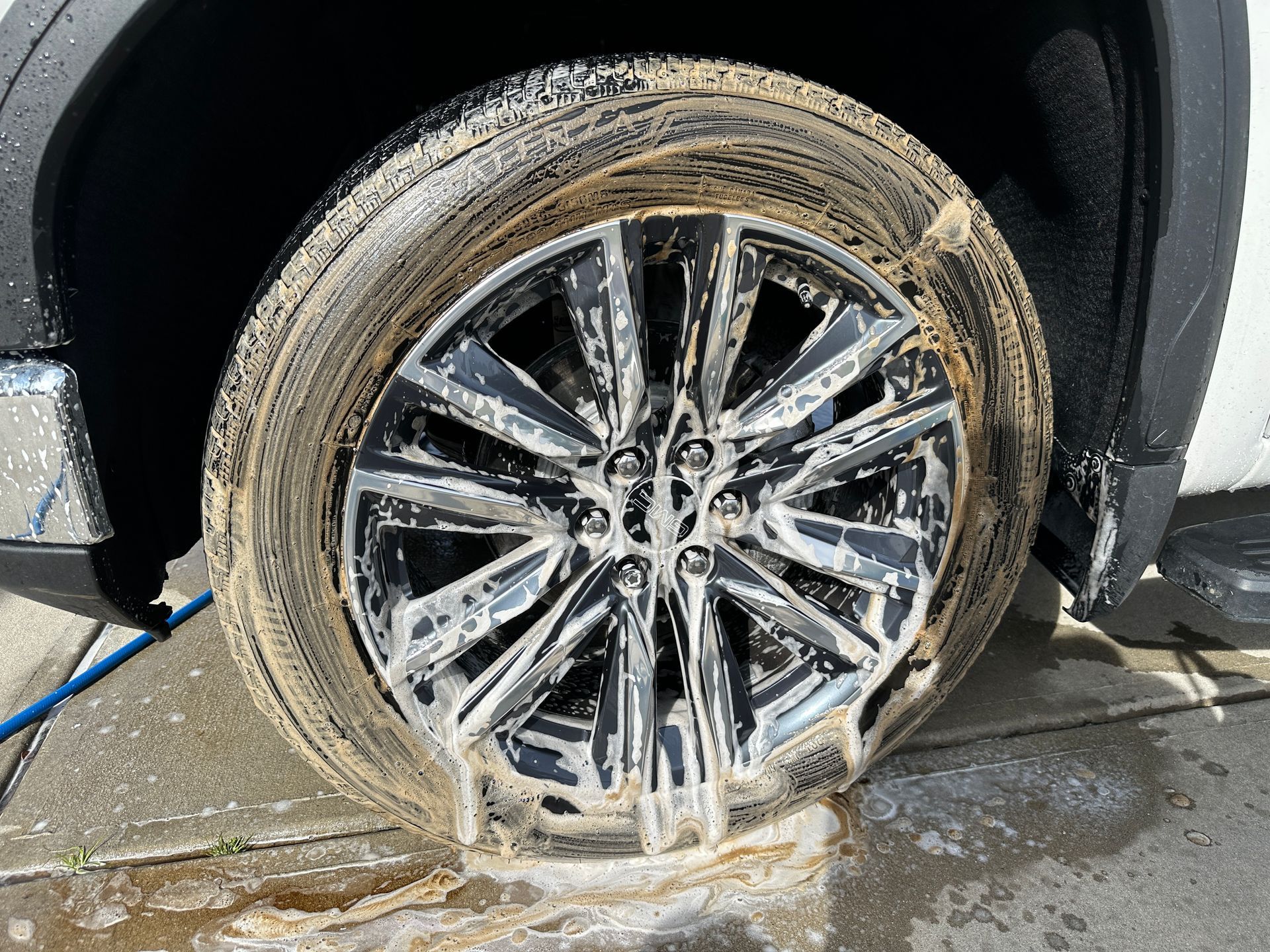 Car wheel covered in foamy soap suds during a car wash.