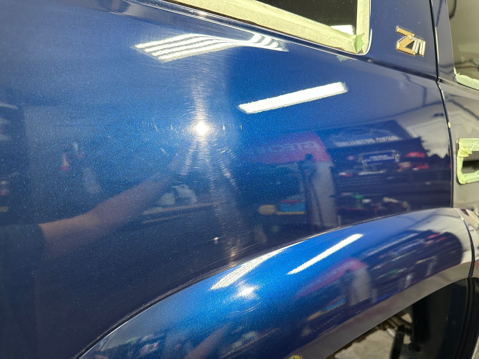 Blue car paint with visible speckles, reflecting interior lights. Bodywork shows some imperfections.