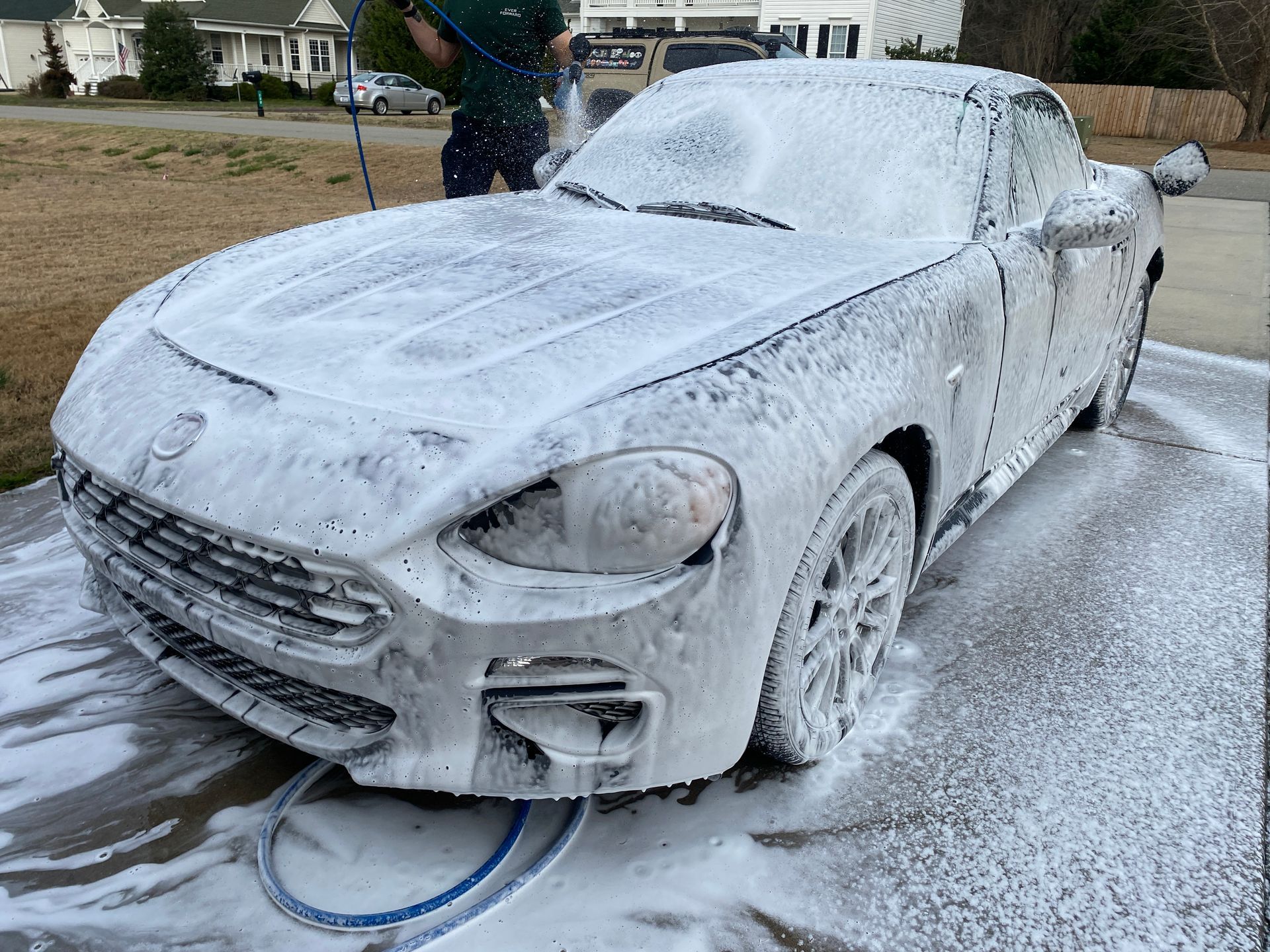 Car covered in white foam being washed outdoors.