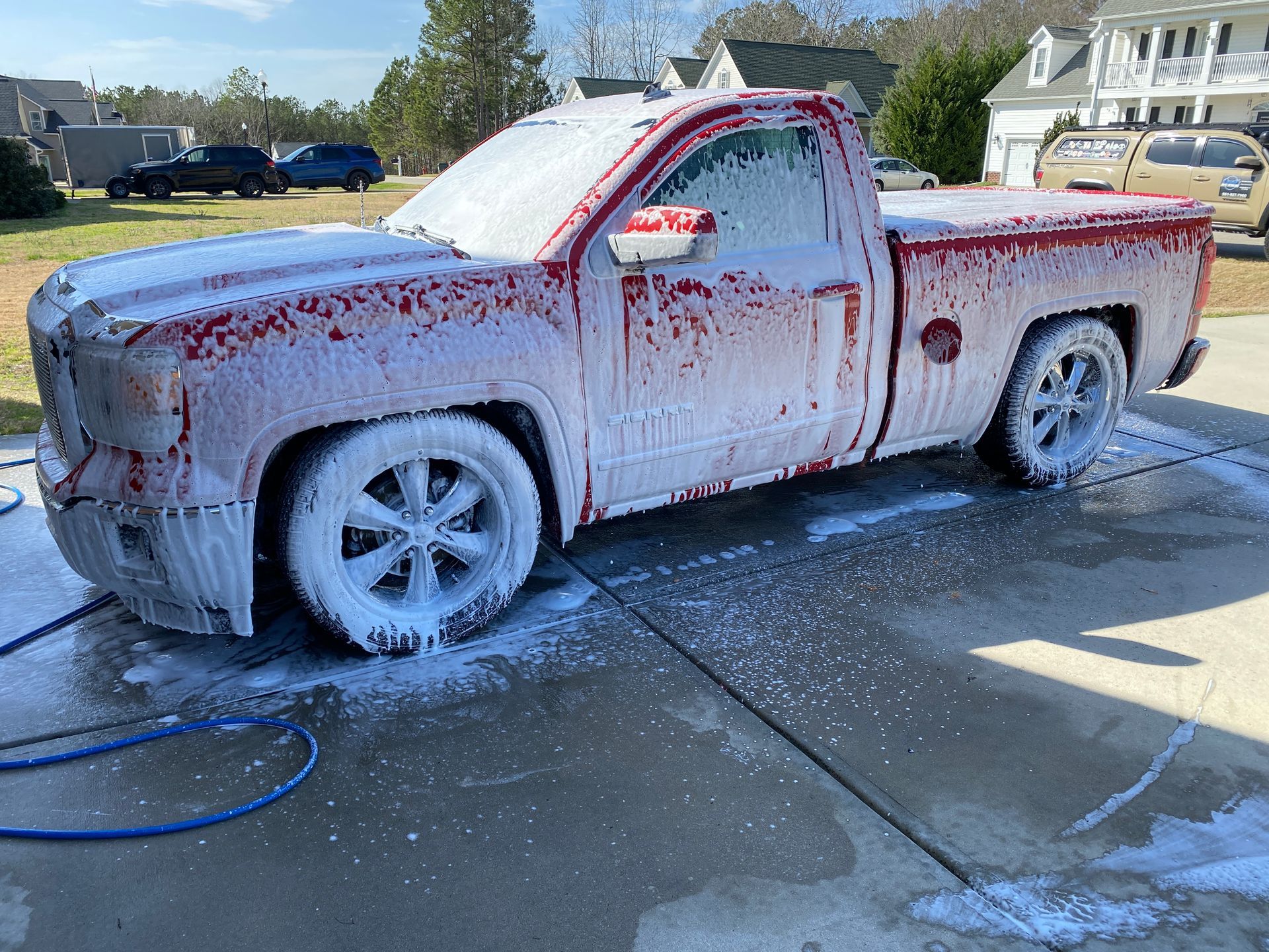 Red pickup truck covered in white foam, parked in driveway.