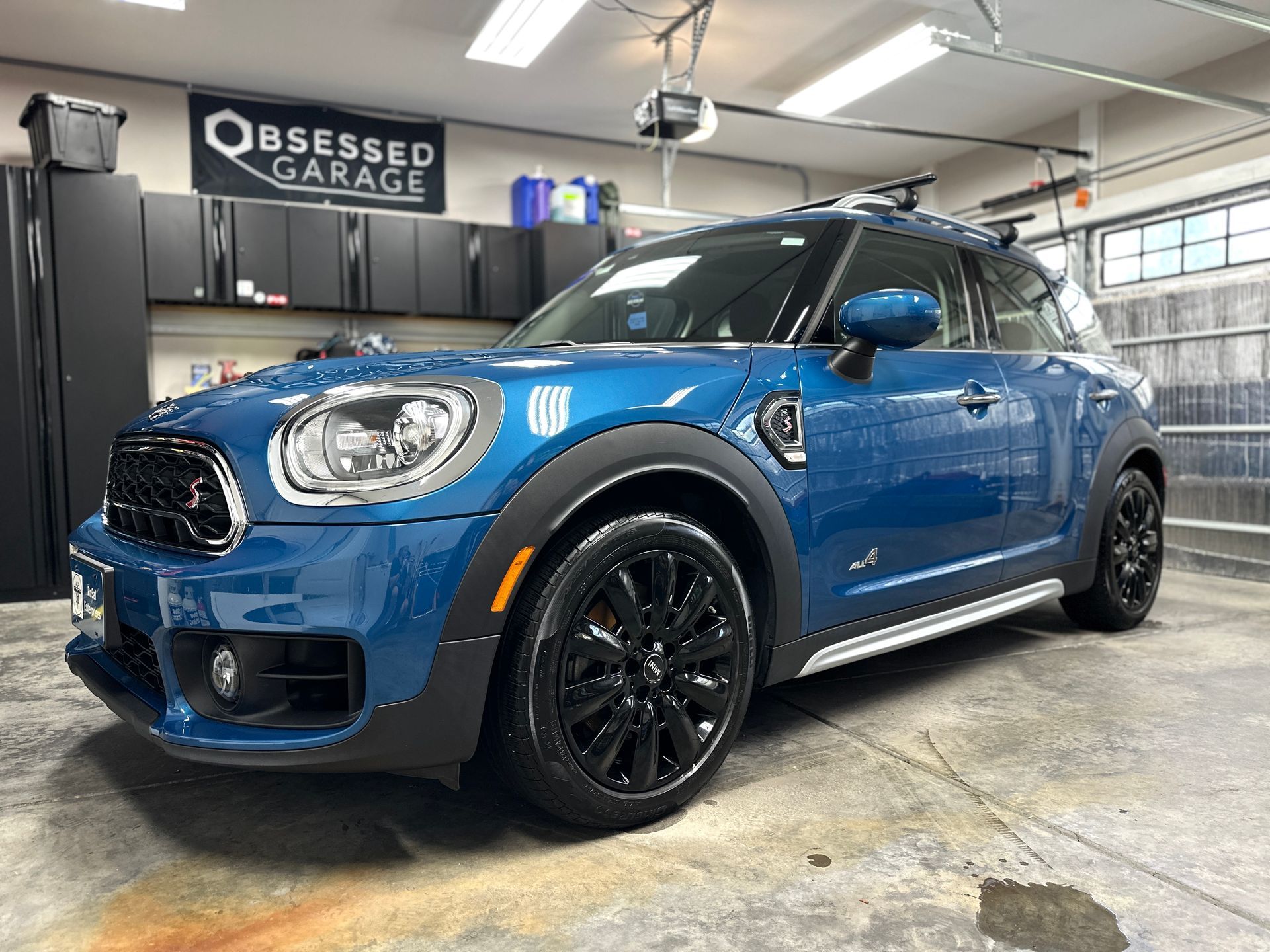Blue Mini Cooper SUV parked in a garage, with black wheels. 