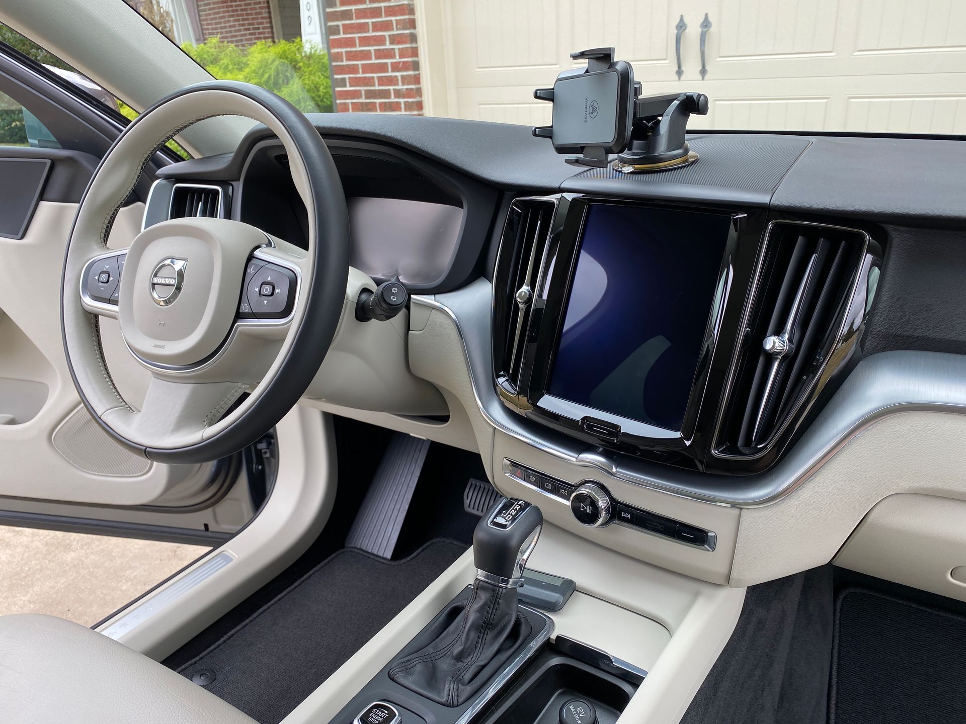Beige and black Volvo car interior with a touchscreen, steering wheel, and gear shift.