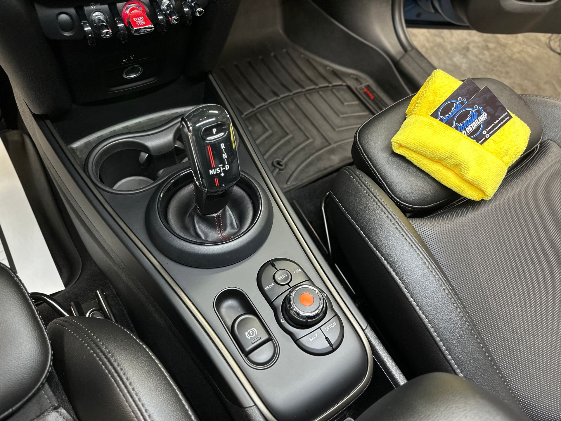 Interior car console with gearshift, cup holders, and control knob; yellow cloth on seat.