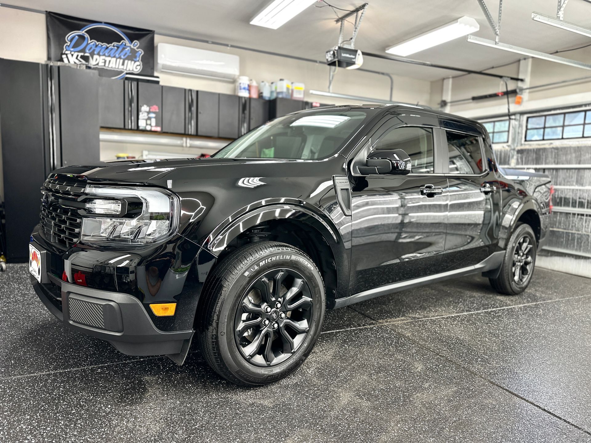 Black Ford Maverick pickup truck parked in a garage with glossy flooring.