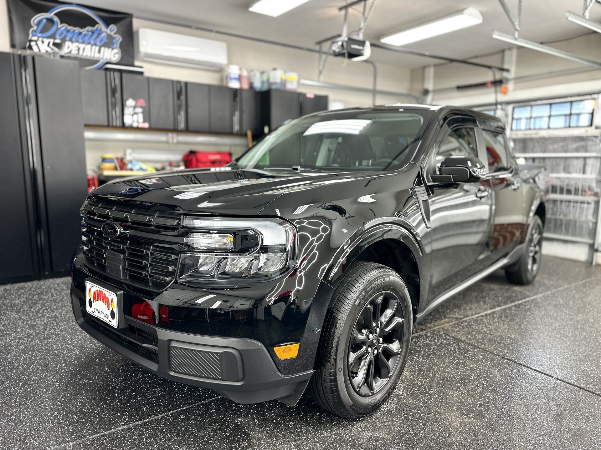 Black Ford Maverick pickup truck in a well-lit garage, parked on a speckled floor.