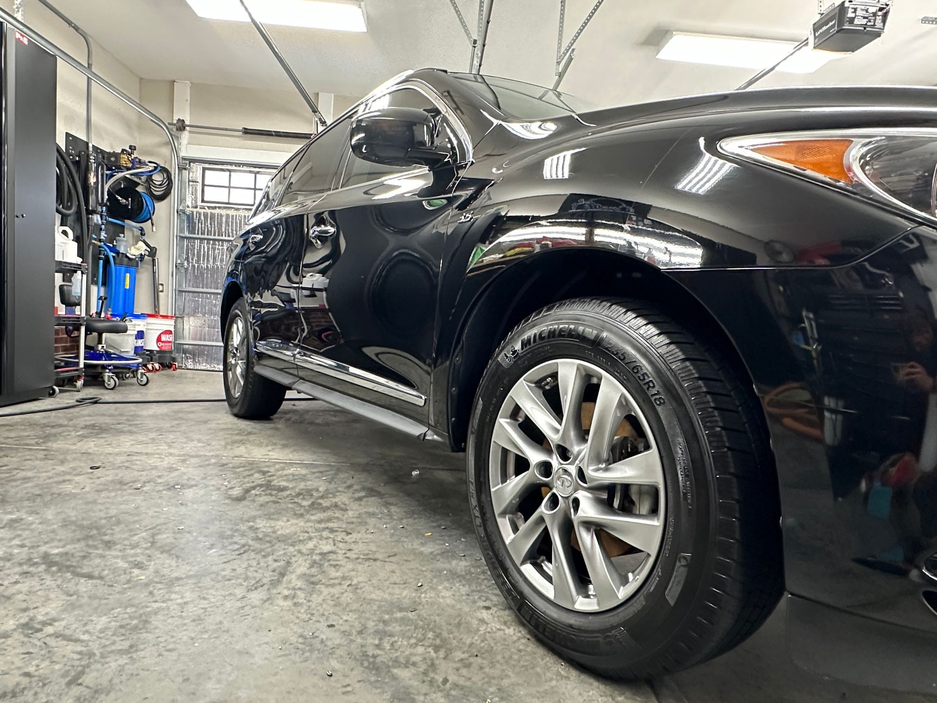 Black car in a garage, shiny exterior, silver rims, tire in focus.