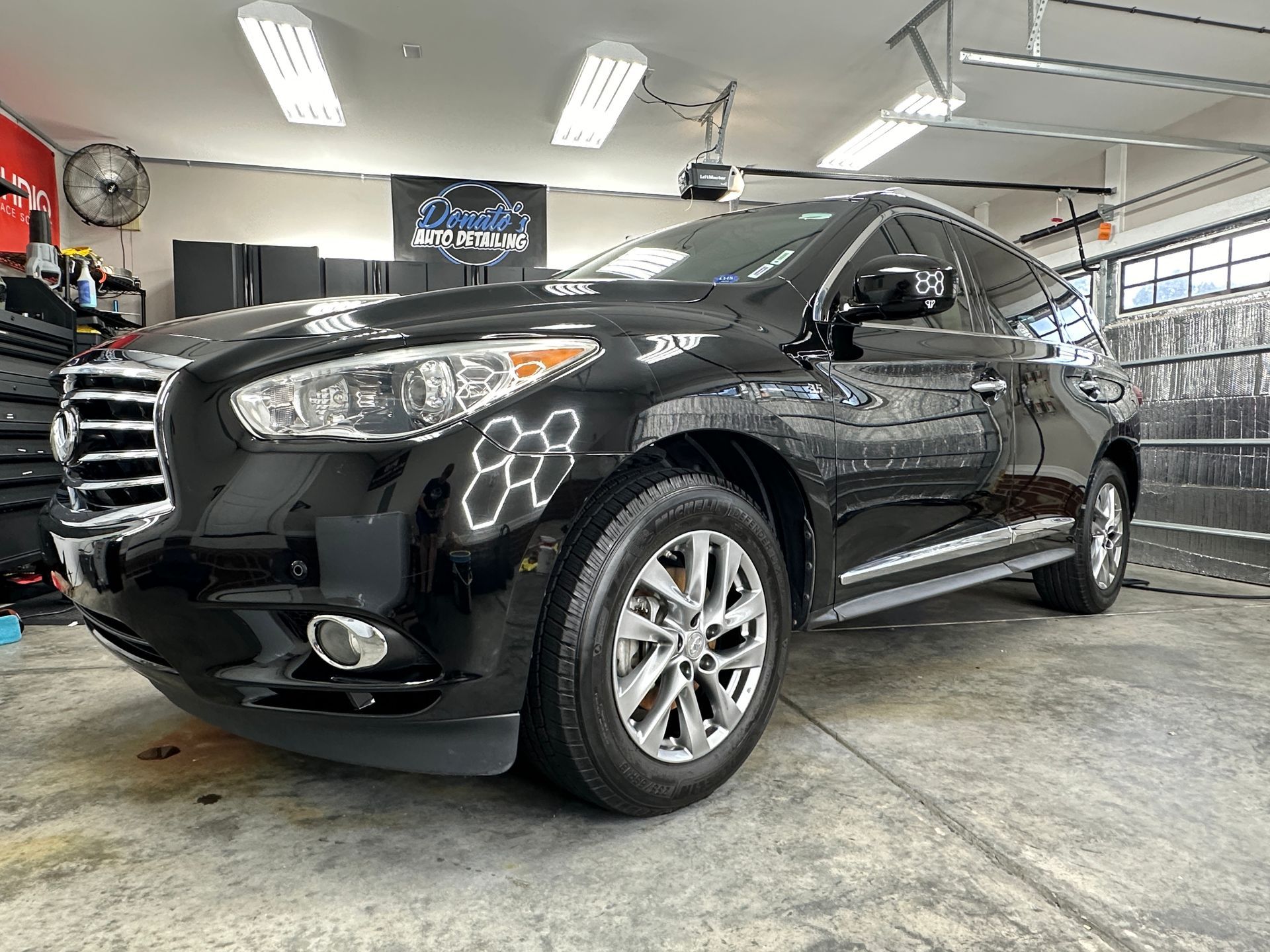 Black SUV parked in a garage with bright lights, shiny wheels, and a reflection.