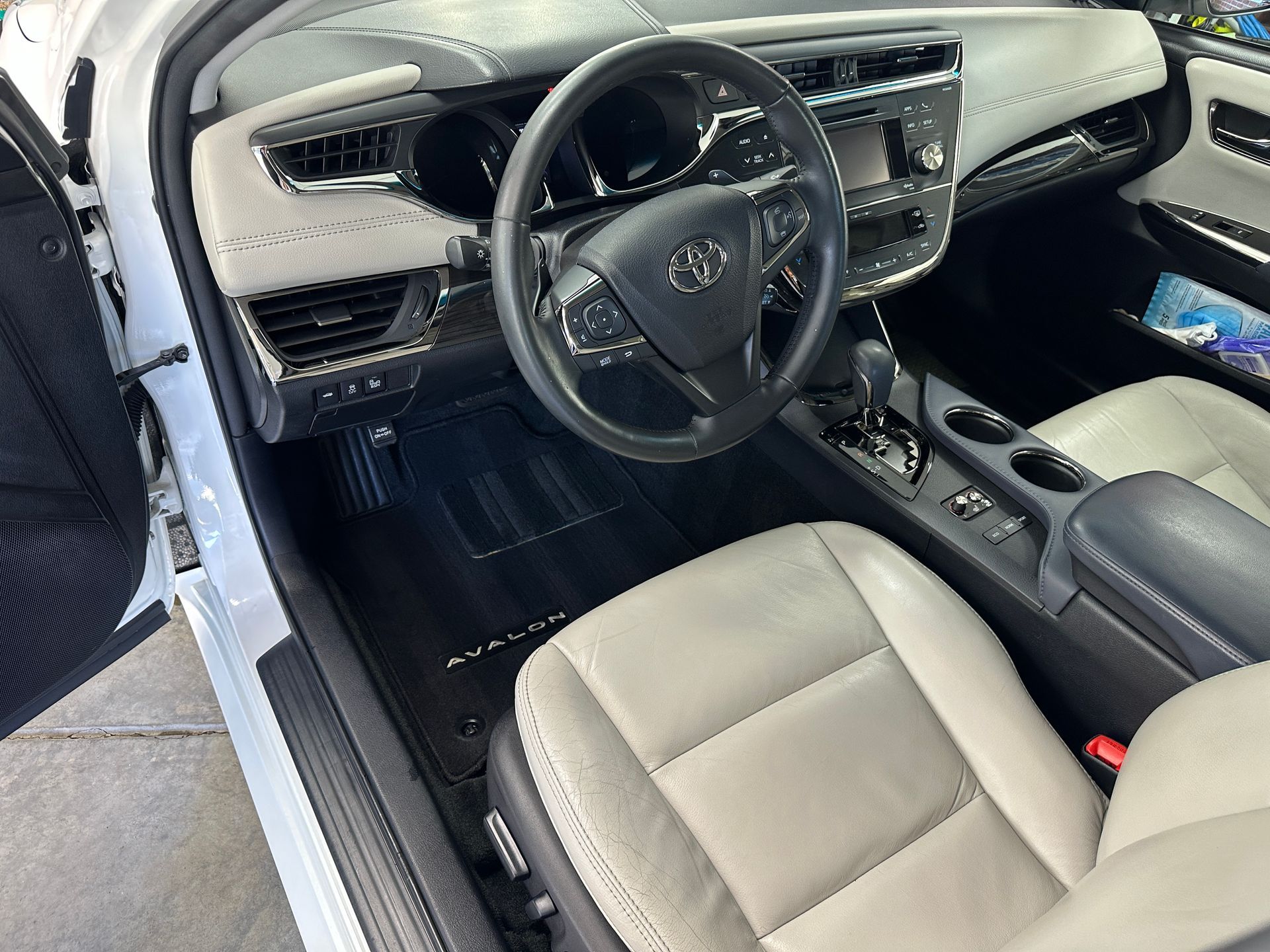 Interior of a white Toyota Avalon. Black steering wheel and dashboard, gray leather seats, black floor mats.